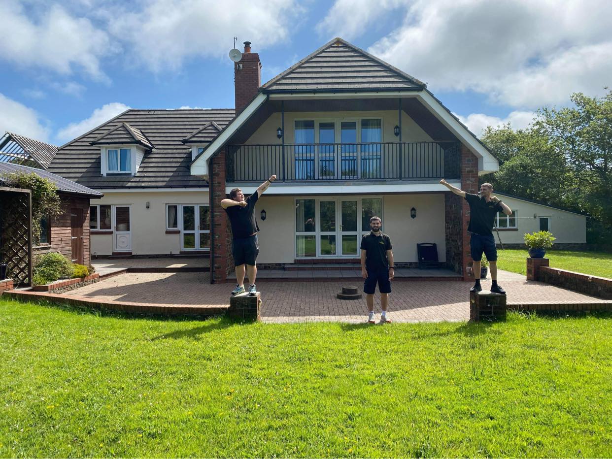 Two children standing on a lawn in front of a large house with a balcony and blue sky.