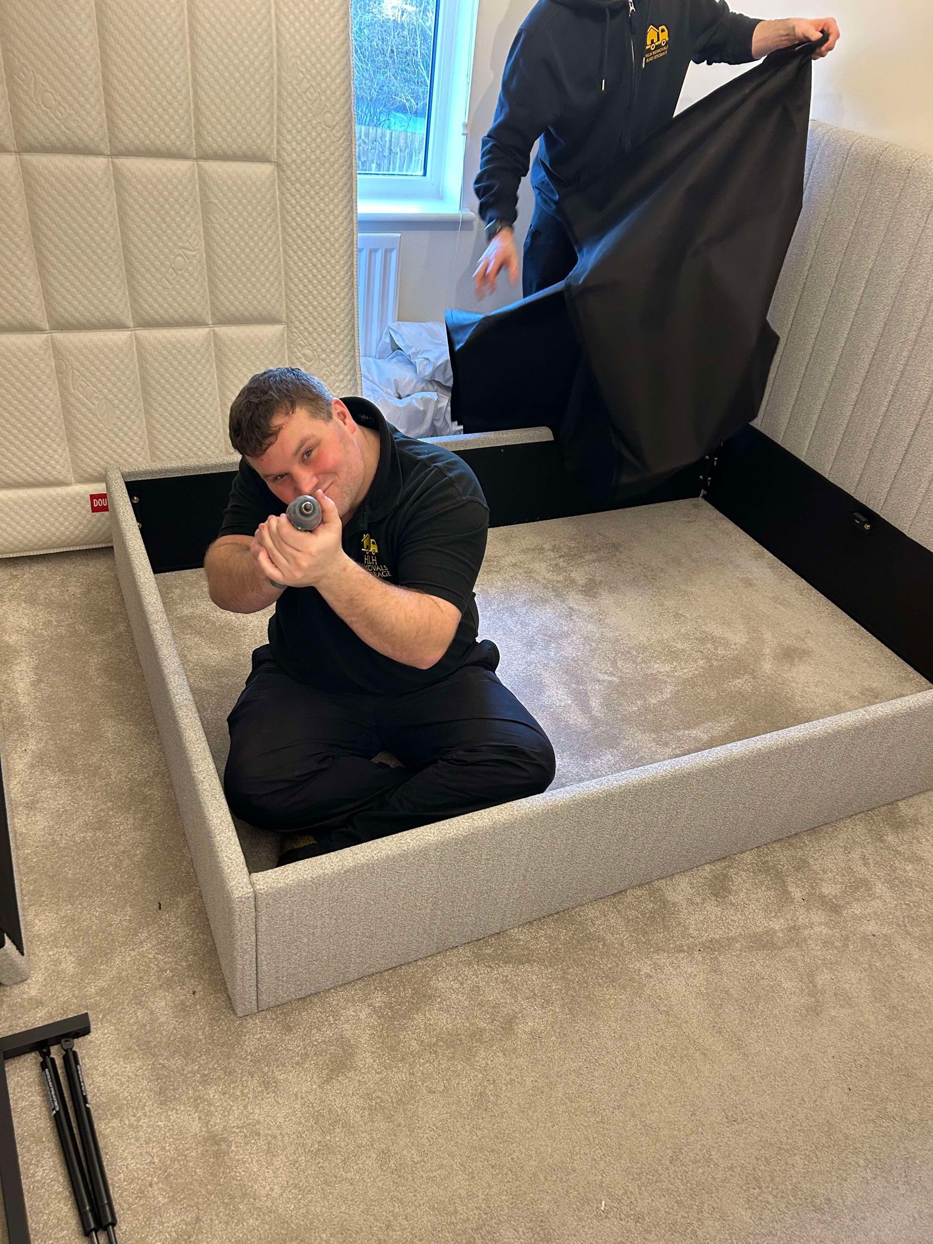 Man kneeling in a carpeted room while another person holds open a black fabric backdrop.