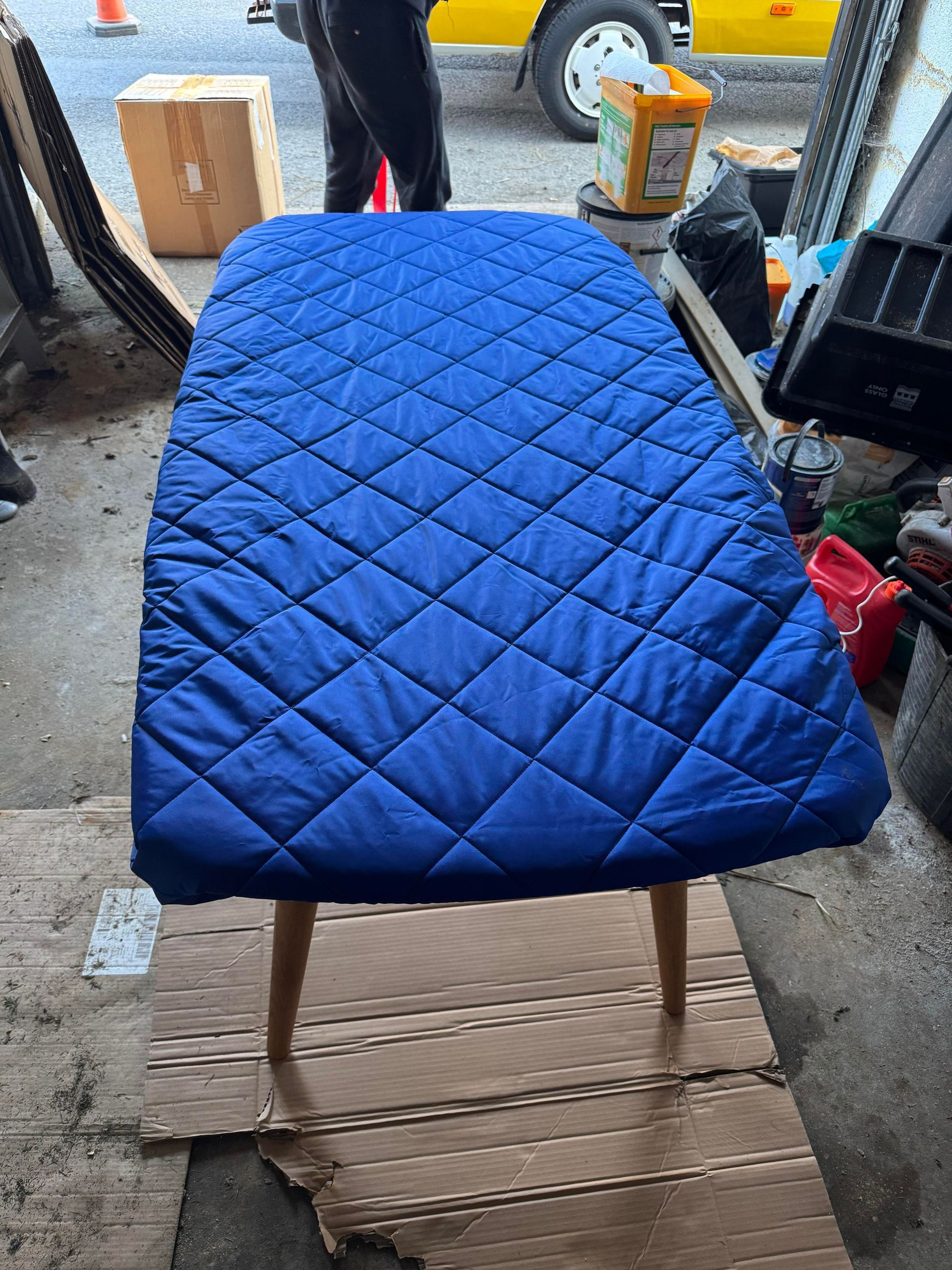 Blue quilted cushion on a chair in a garage, with a person and vehicle in the background.