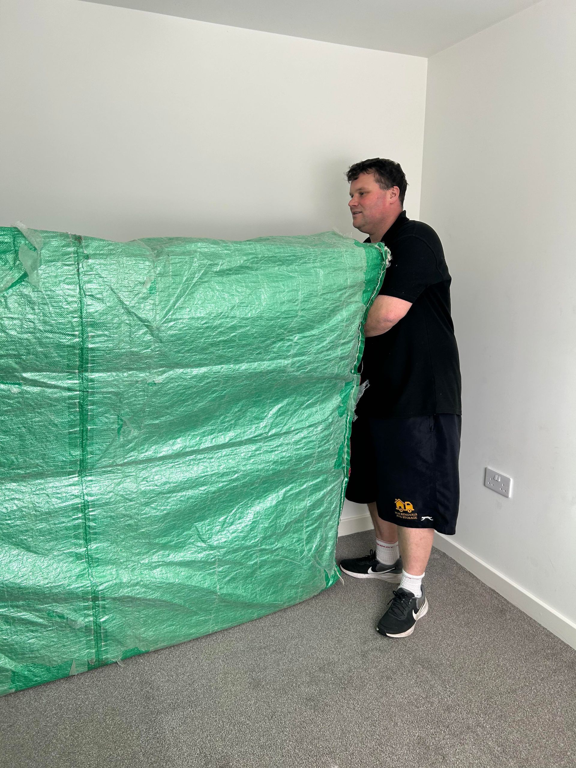 Person moving a large green tarp in a carpeted room with white walls