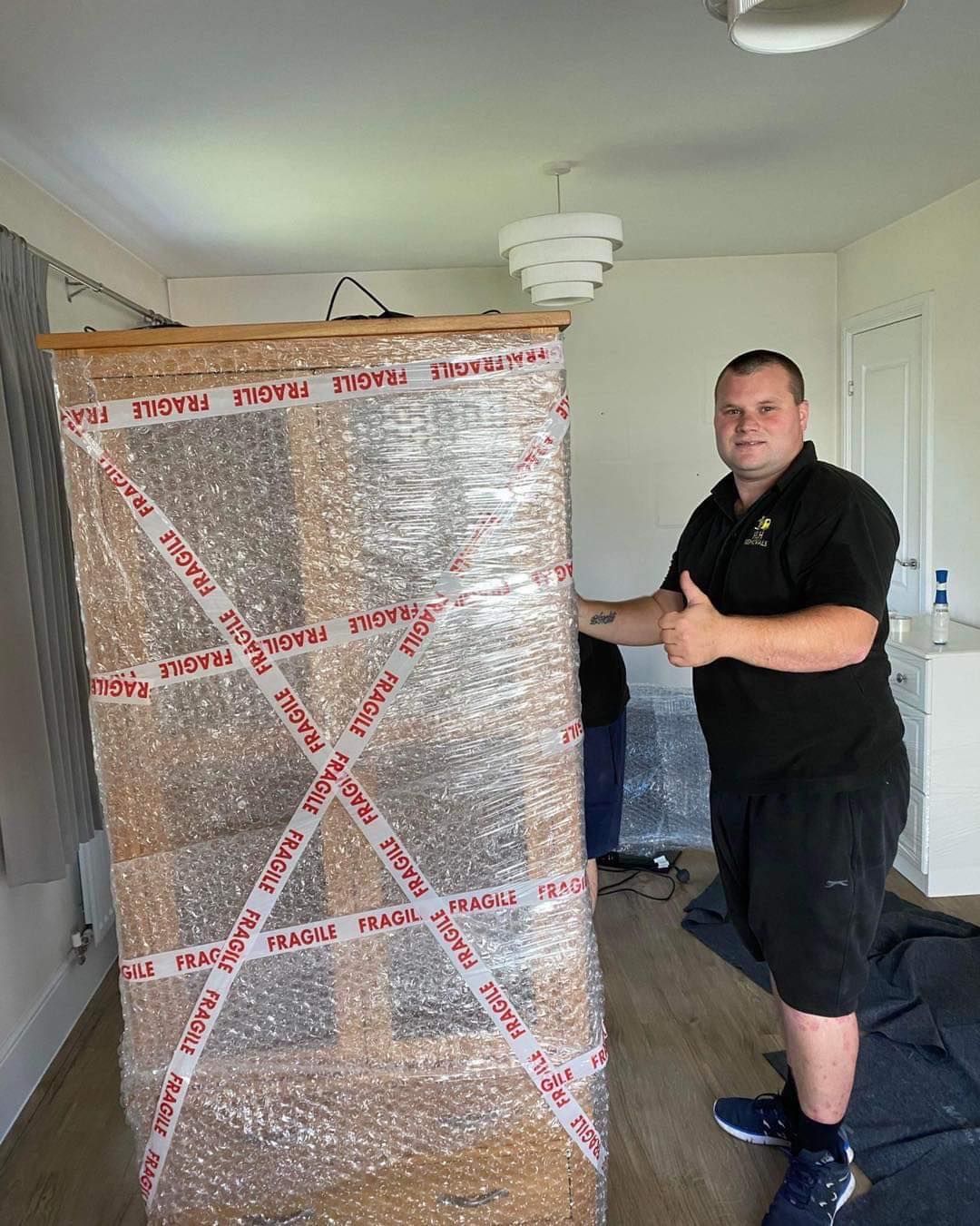Man standing beside a large box wrapped in protective plastic and tape inside a room