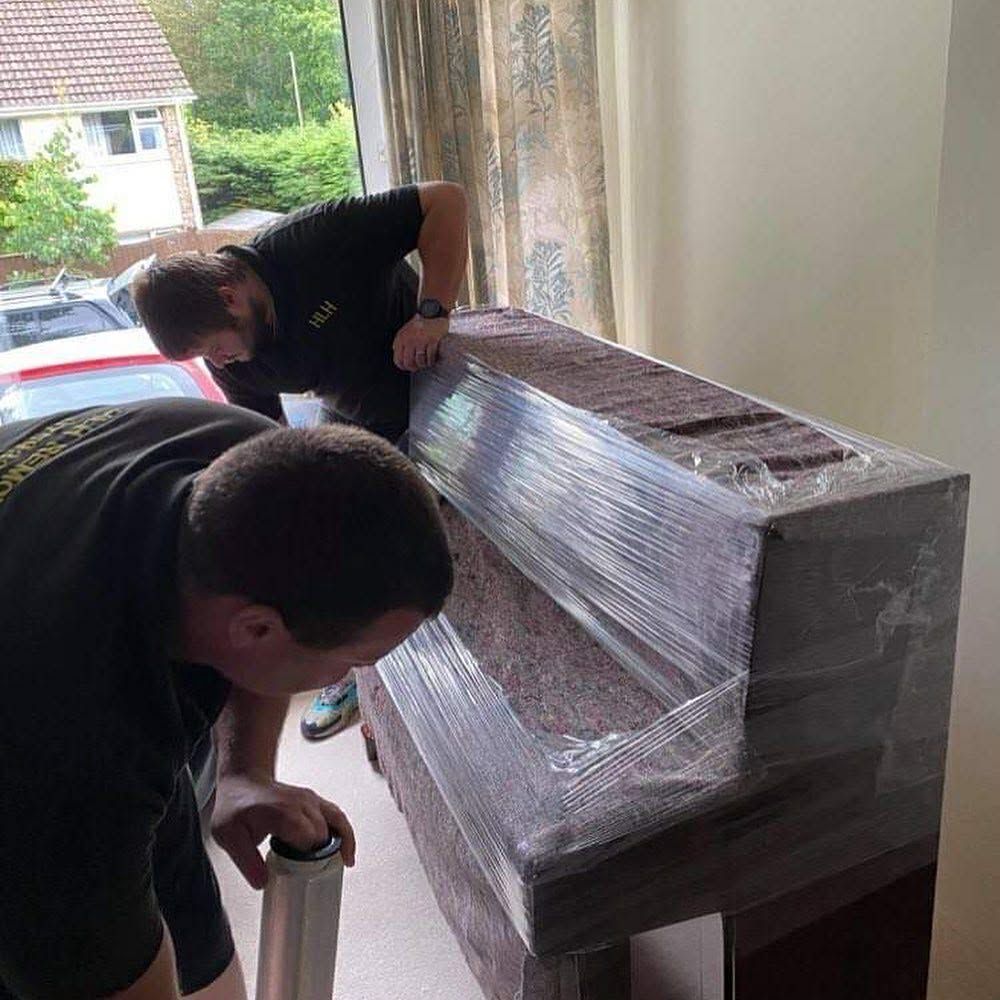 Two movers wrapping a dark wooden cabinet in plastic near a doorway