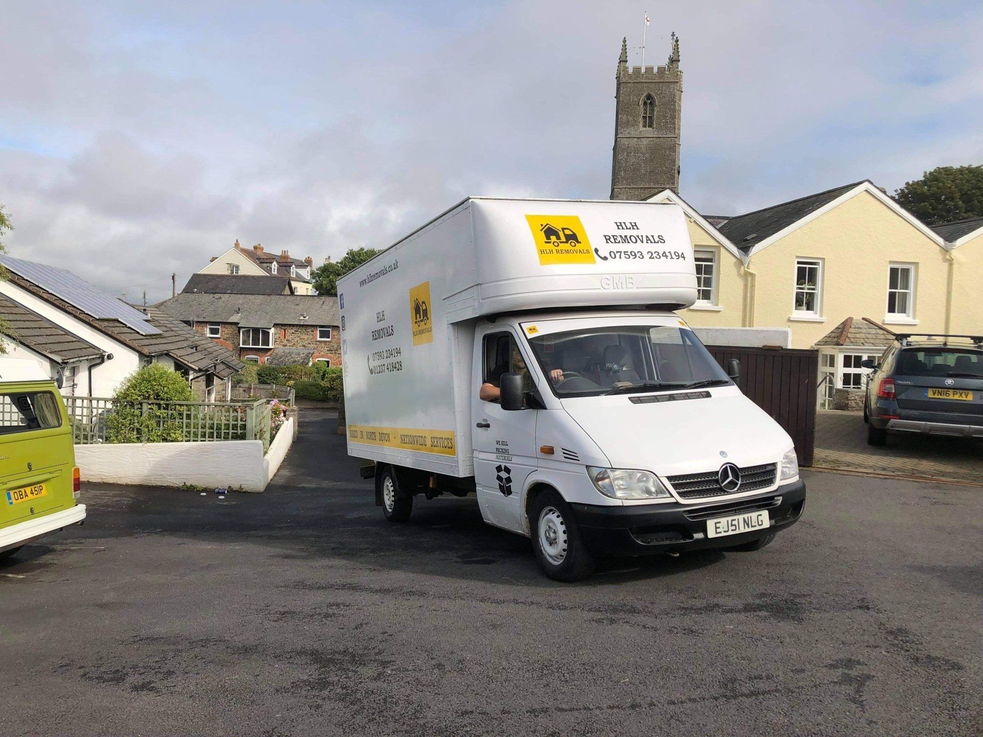 White delivery van turning on a residential street near stone houses and a church tower