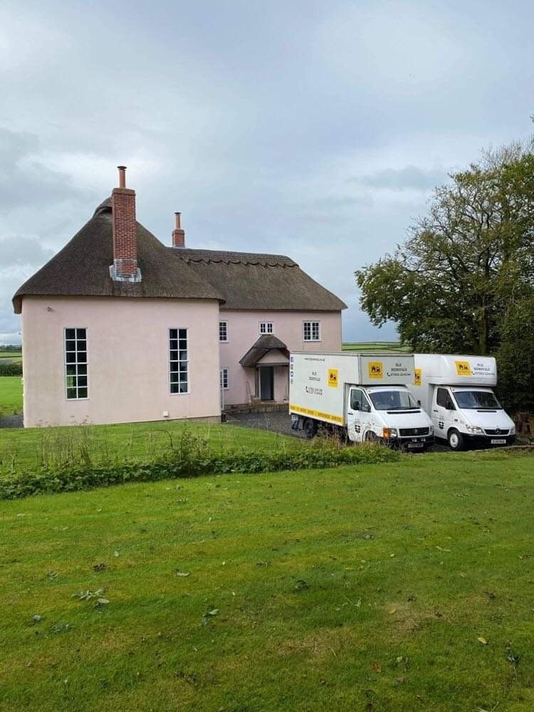 Pink house with lawn, and two white delivery vans parked by an arched doorway
