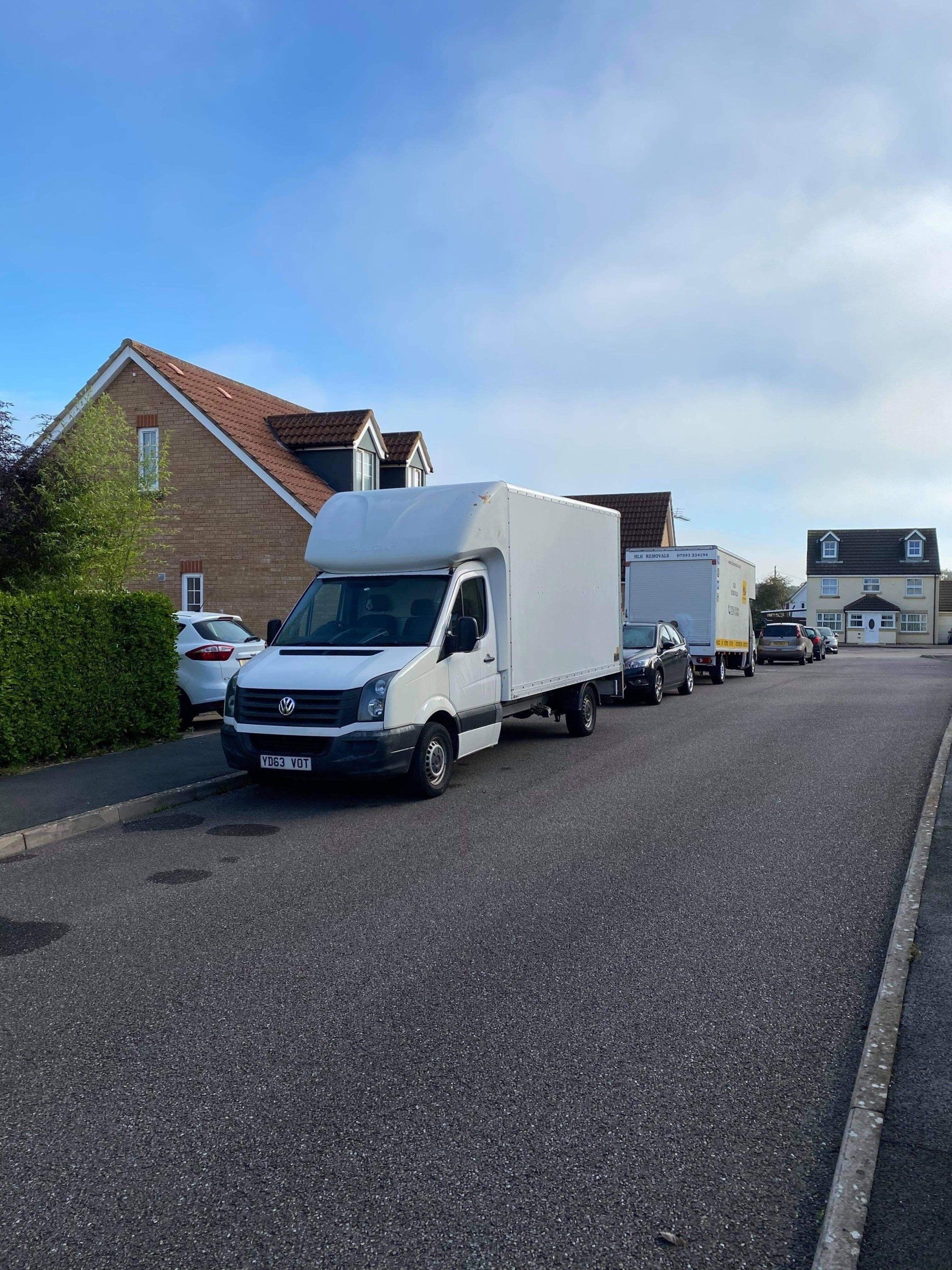White delivery vans parked along a residential street beside brick houses under a blue sky.