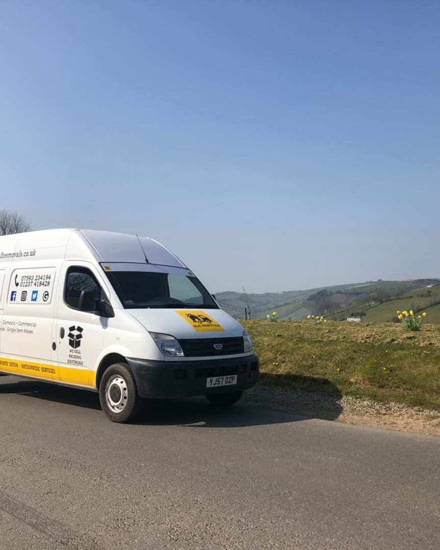 White delivery van parked on a rural roadside beside open fields under a clear blue sky
