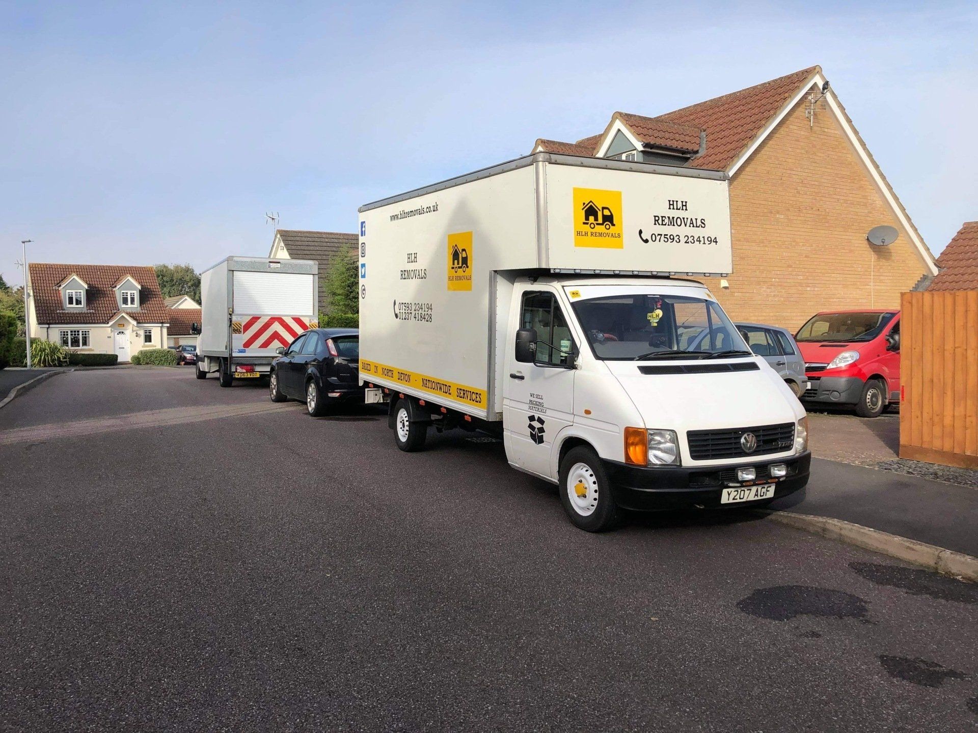 White delivery van parked on a suburban street beside houses and other vehicles