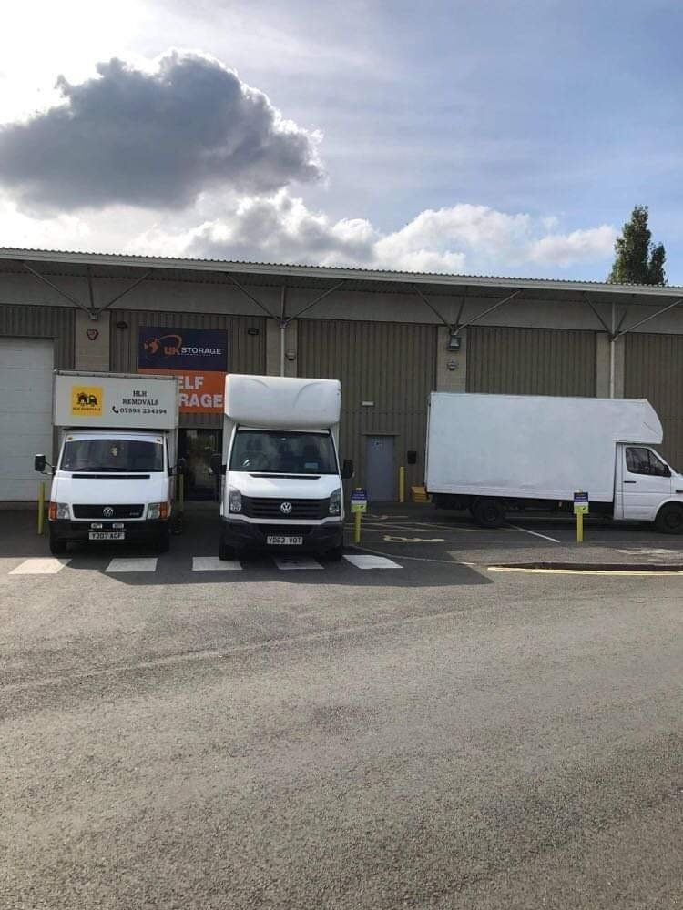 Three white delivery trucks parked outside a warehouse under a cloudy sky.