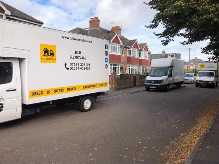 Two moving vans parked on a residential street with houses and autumn leaves