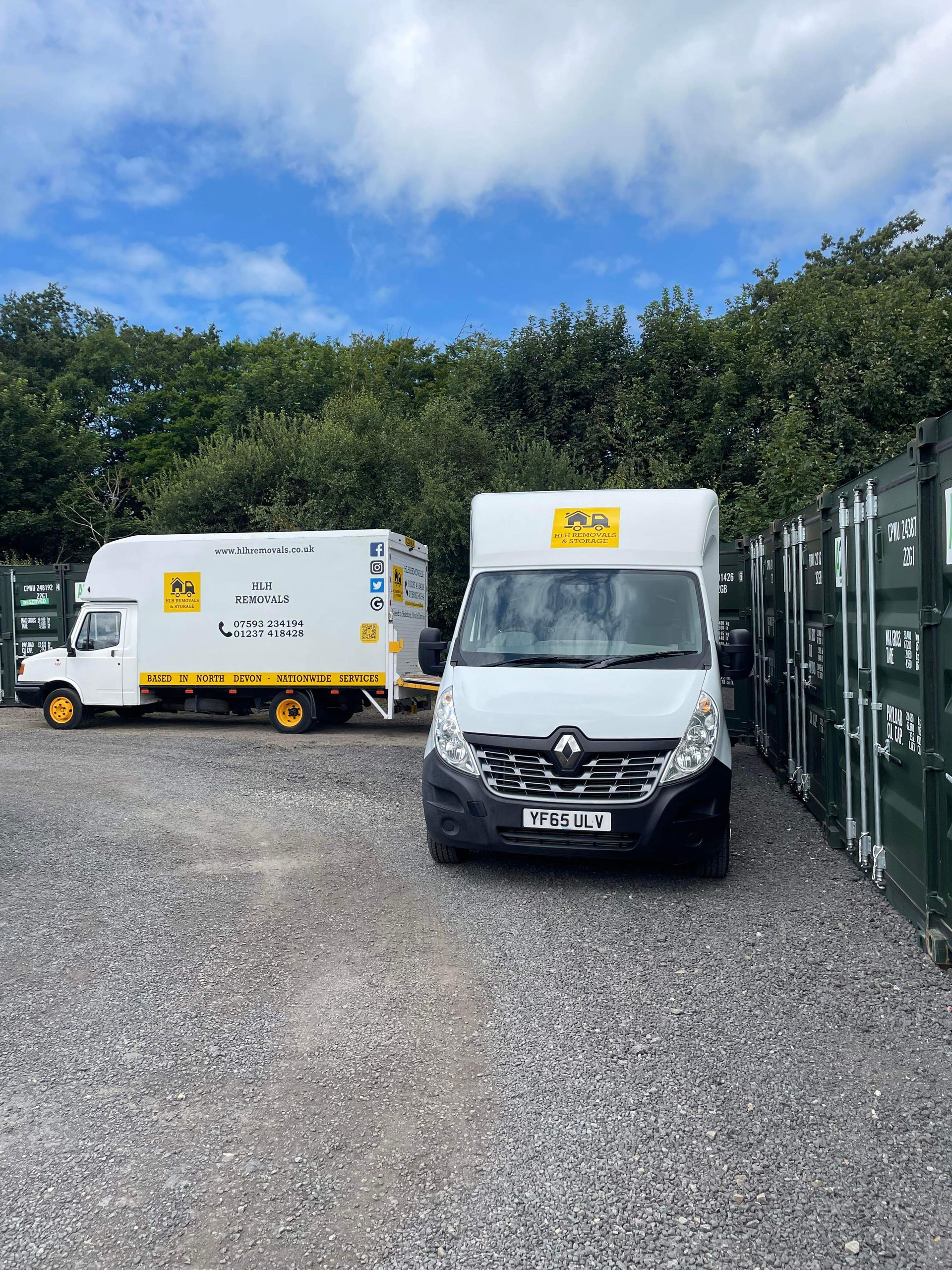 Two white delivery vans in a gravel lot, one facing forward and one side-on, with green trees and a blue sky.