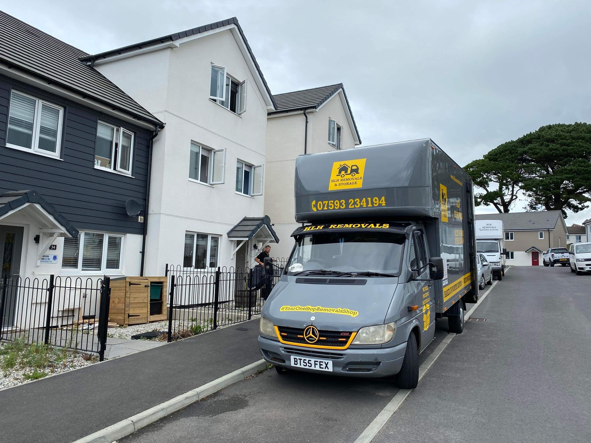Grey Luton van parked on a residential street beside white houses under a cloudy sky