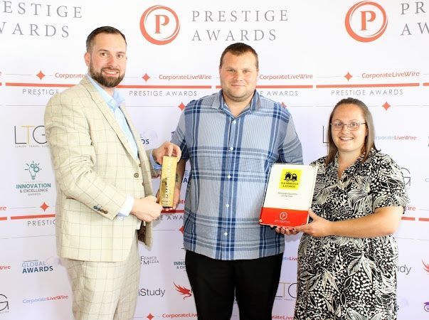 Three people posing at a Prestige Awards event, holding an award trophy and a certificate.