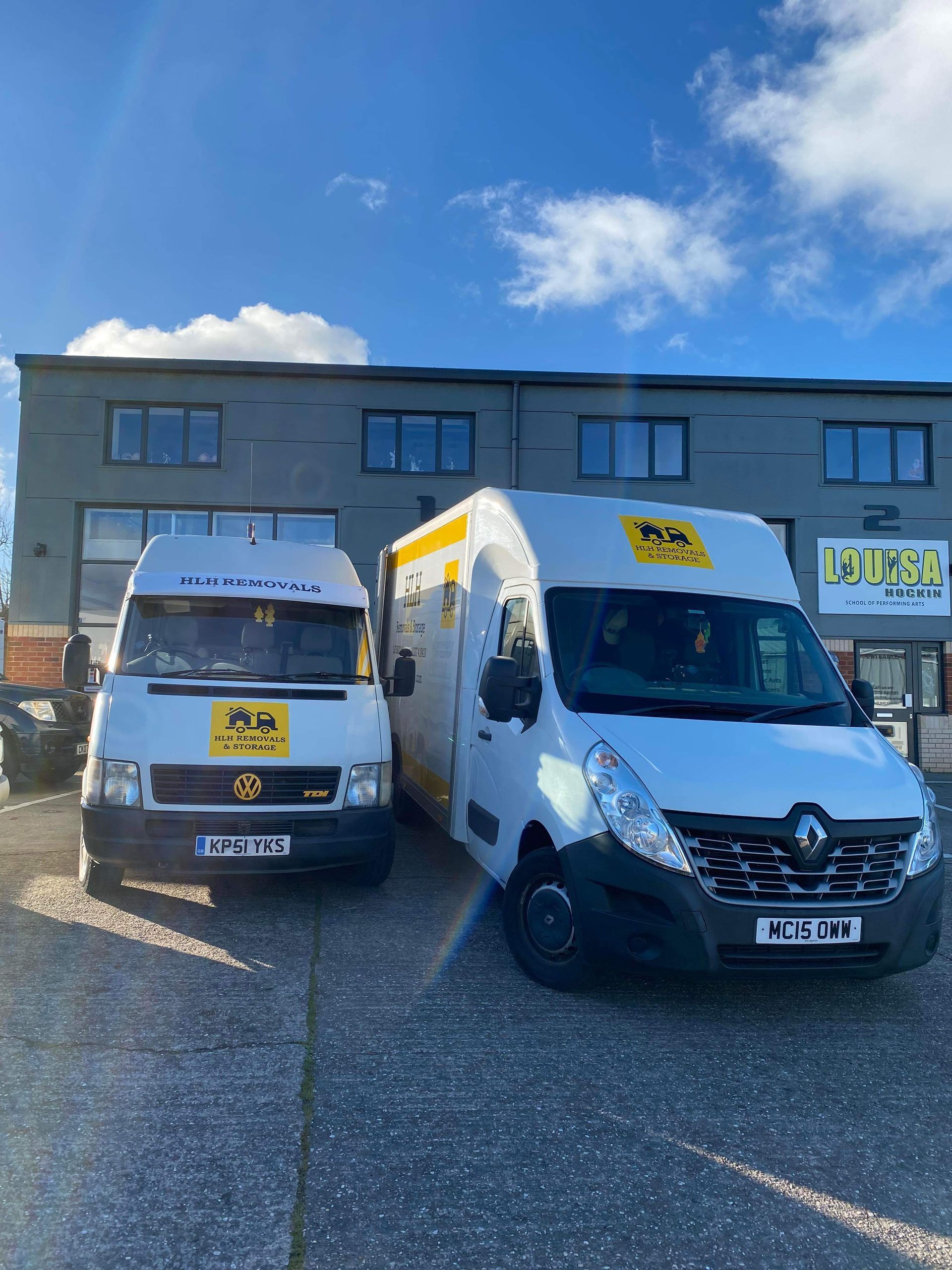 Two white delivery vans parked outside an industrial building under a blue sky