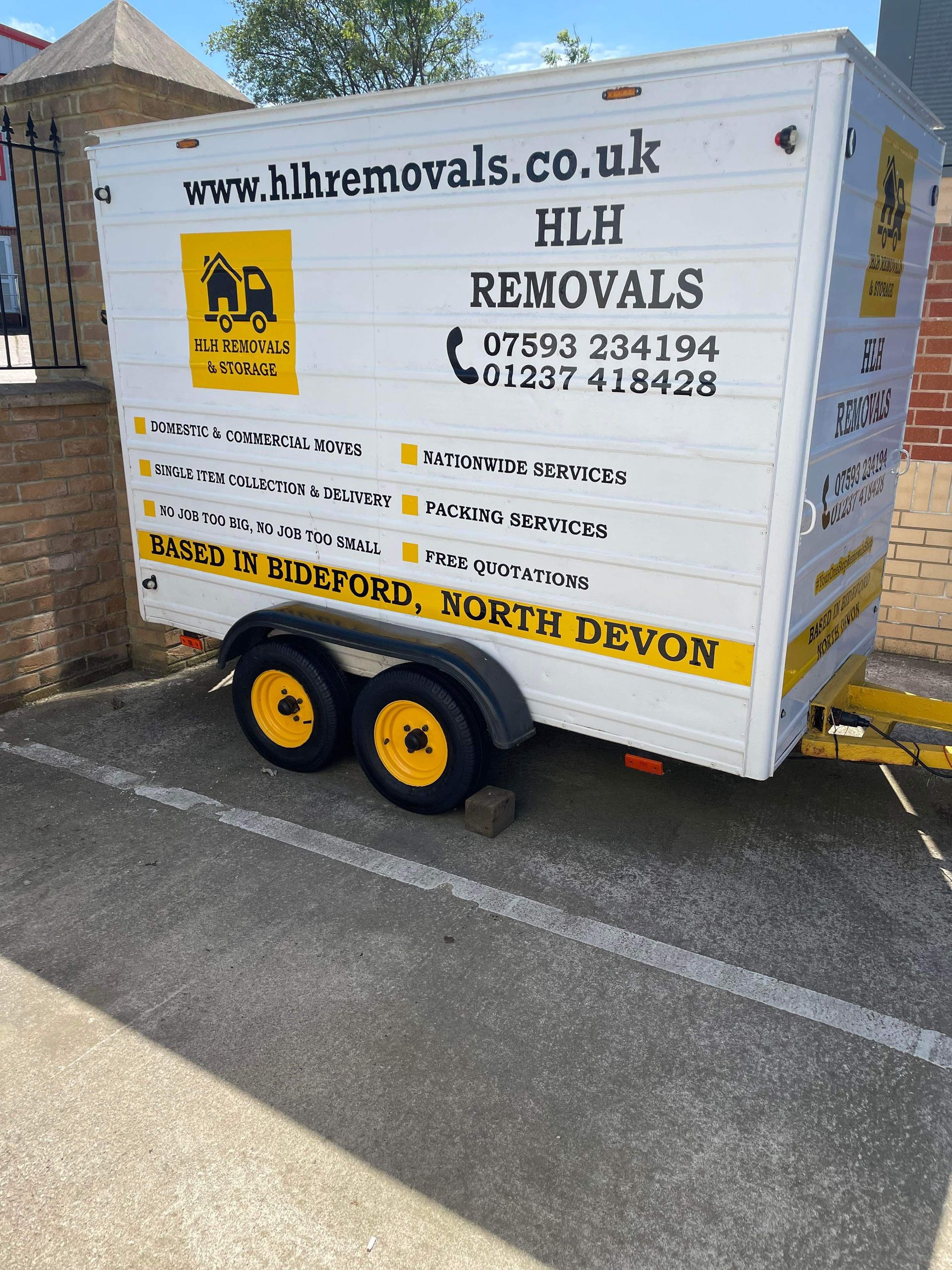 White trailer with “HLH REMOVALS” branding and yellow wheels parked in a lot under sunlight.