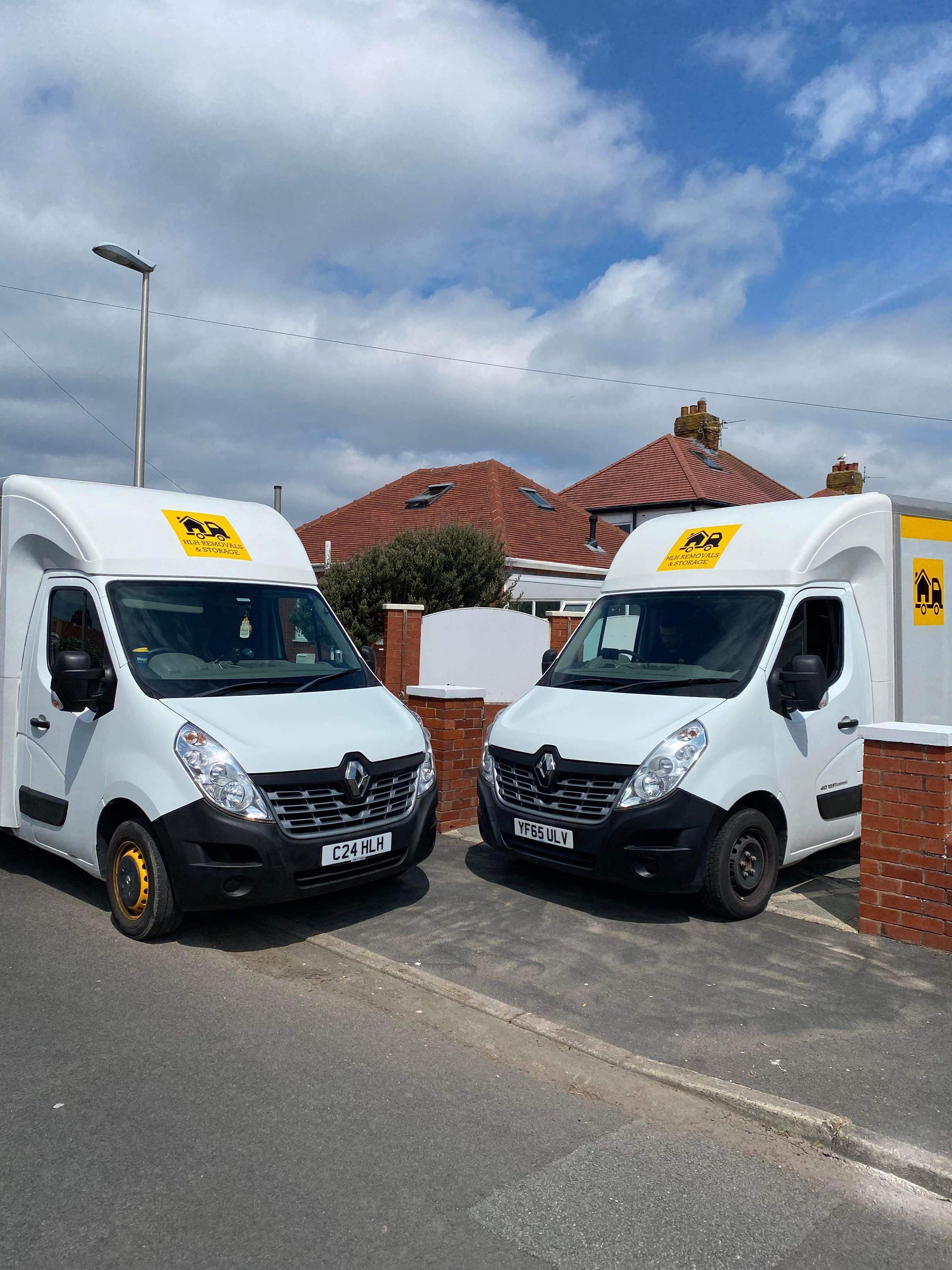 Two white delivery vans parked on a street outside a house with a red tiled roof