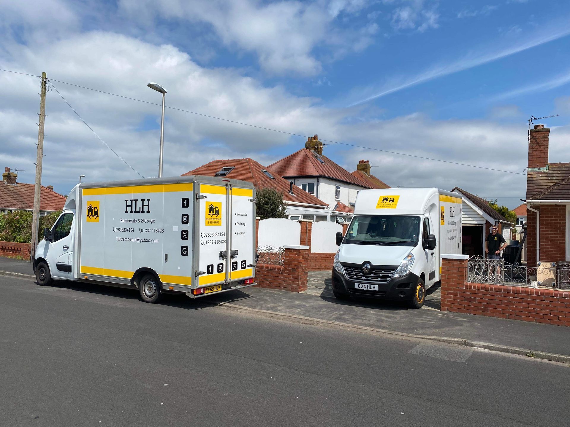Two white delivery vans parked outside suburban brick houses on a sunny street