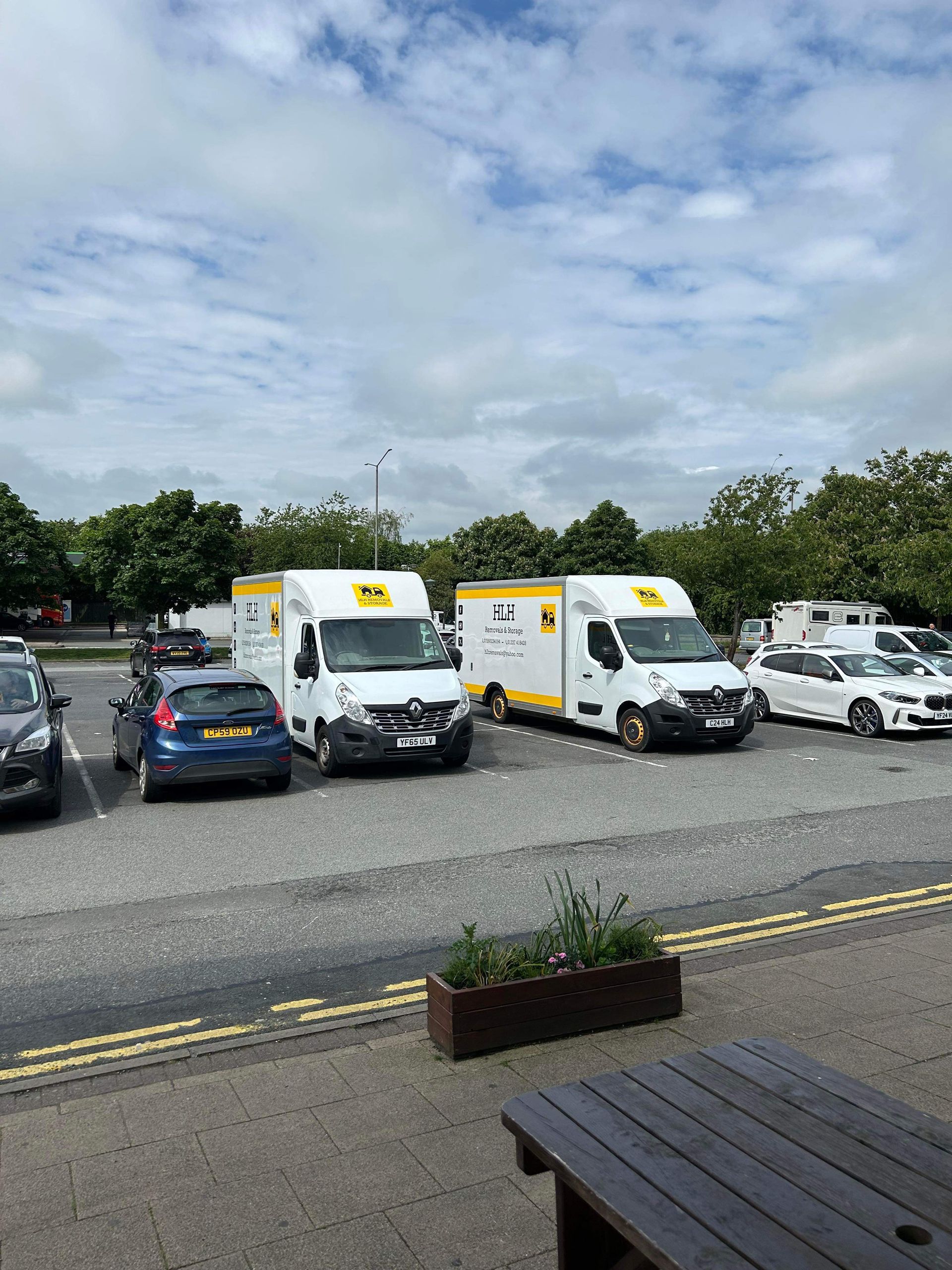 Parking lot with white delivery vans, parked cars, and a cloudy sky over gravel and picnic tables.