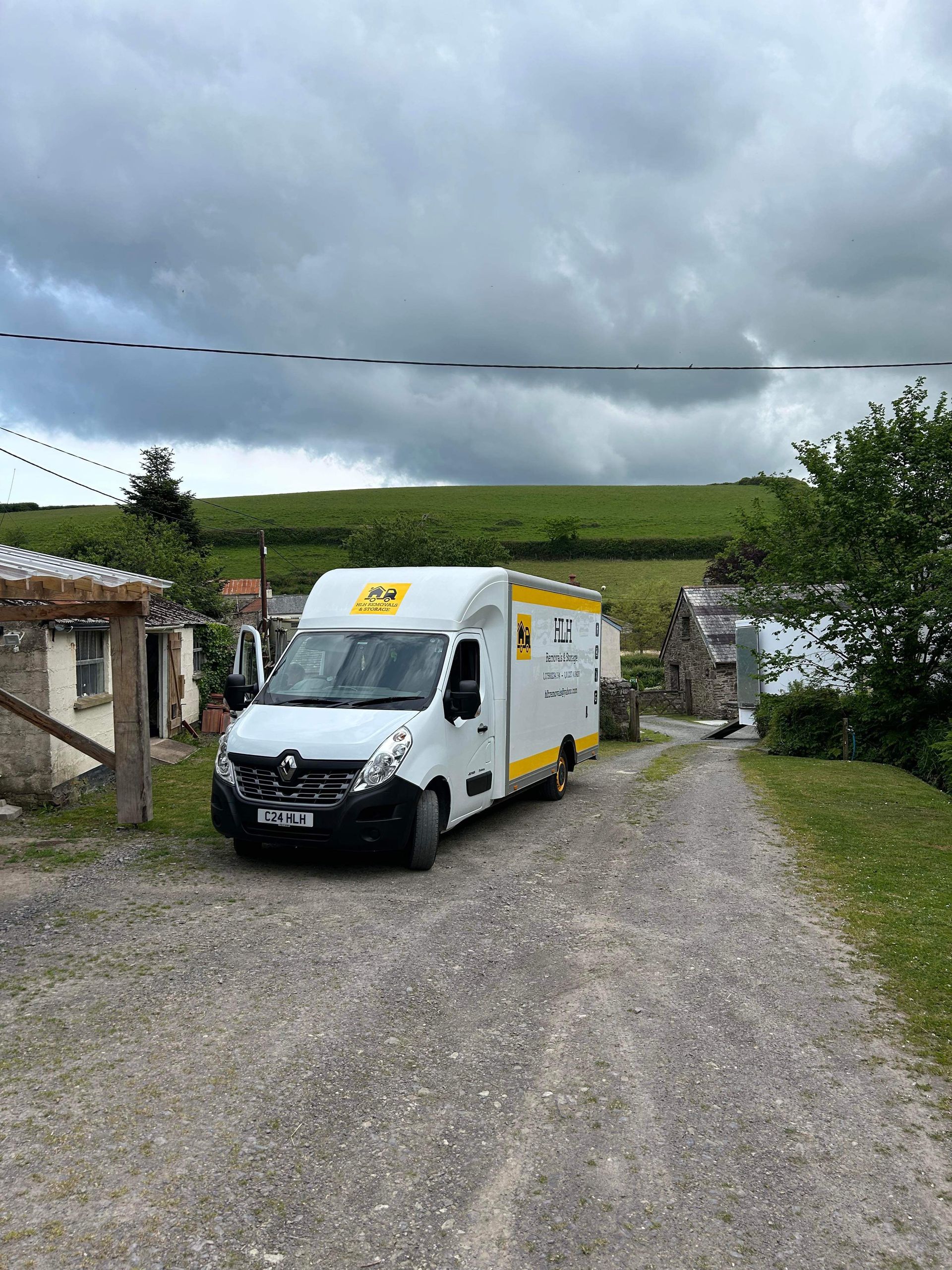 White delivery van parked on a gravel driveway beside houses under a cloudy sky.