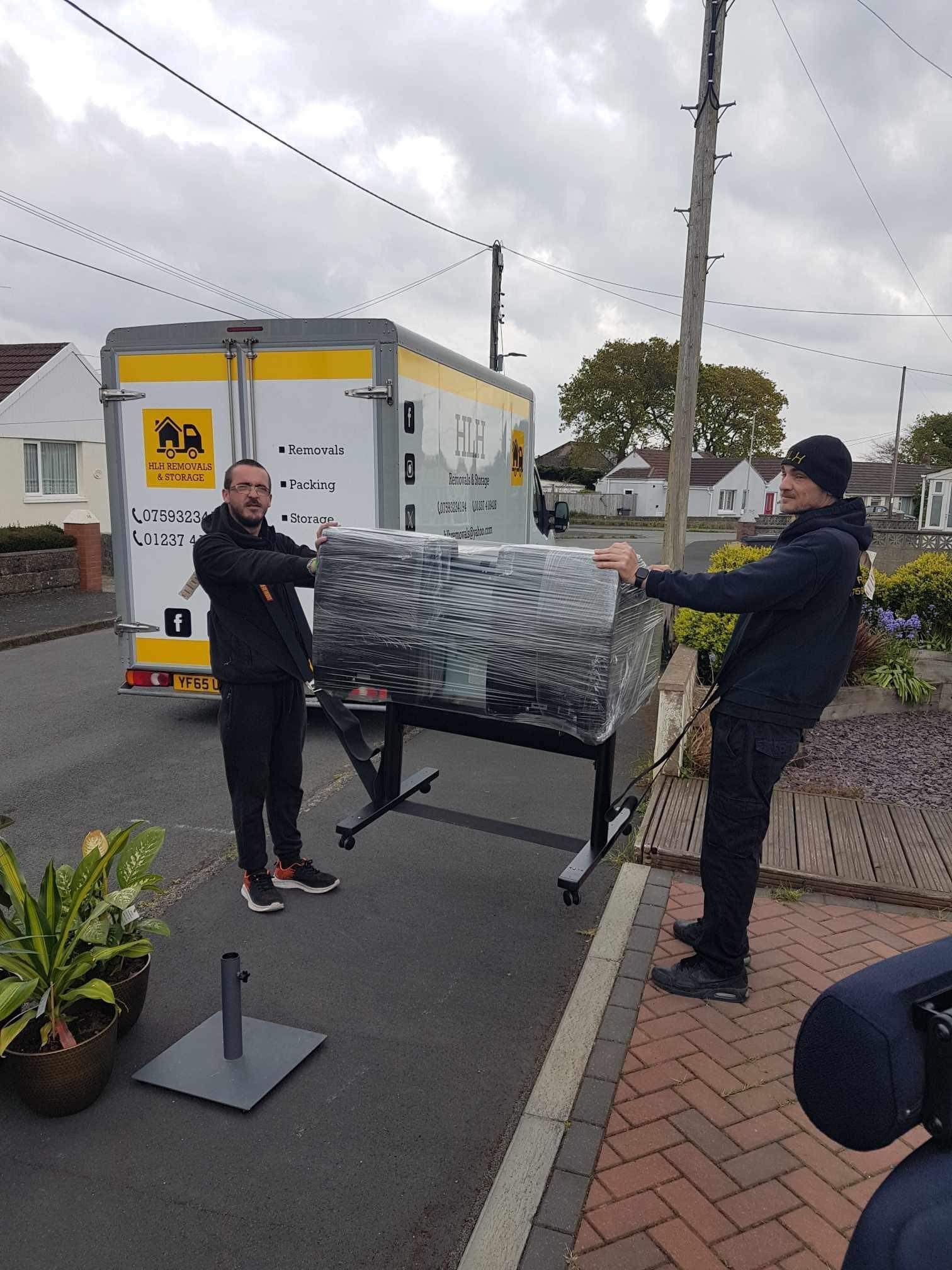 Two workers unloading a wrapped table from a delivery van on a suburban street