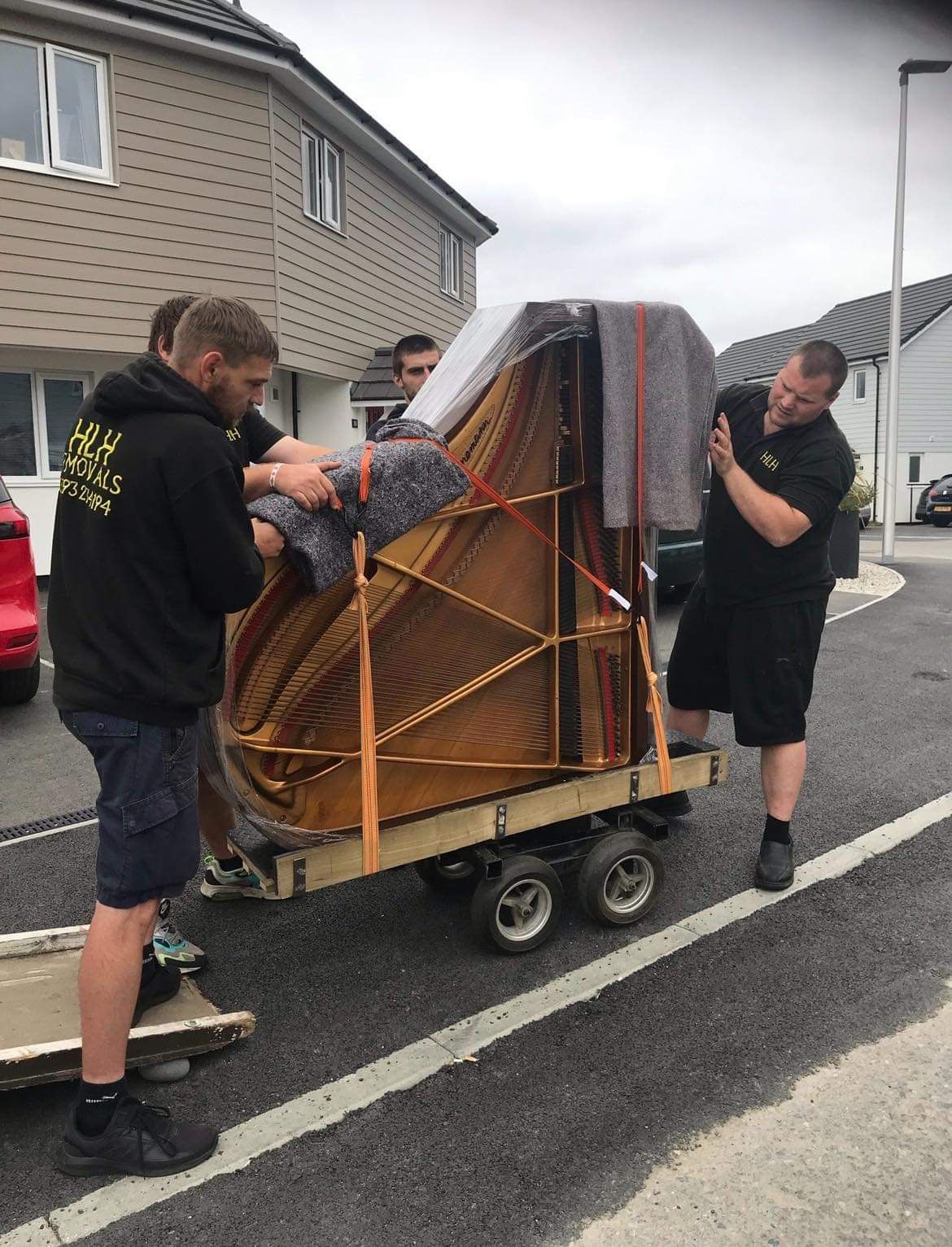 Two men loading a wrapped upright piano onto a dolly on a wet residential street