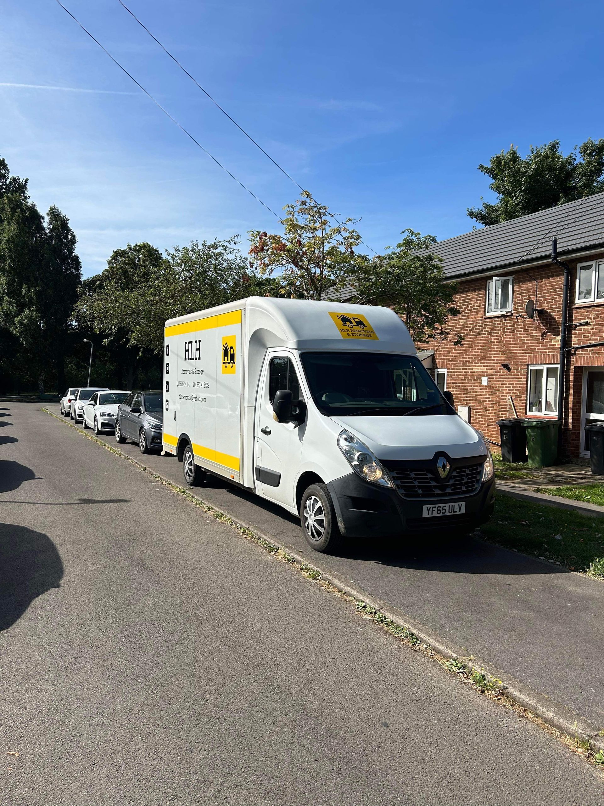 White DHL delivery van parked on a residential street beside brick houses under a clear blue sky