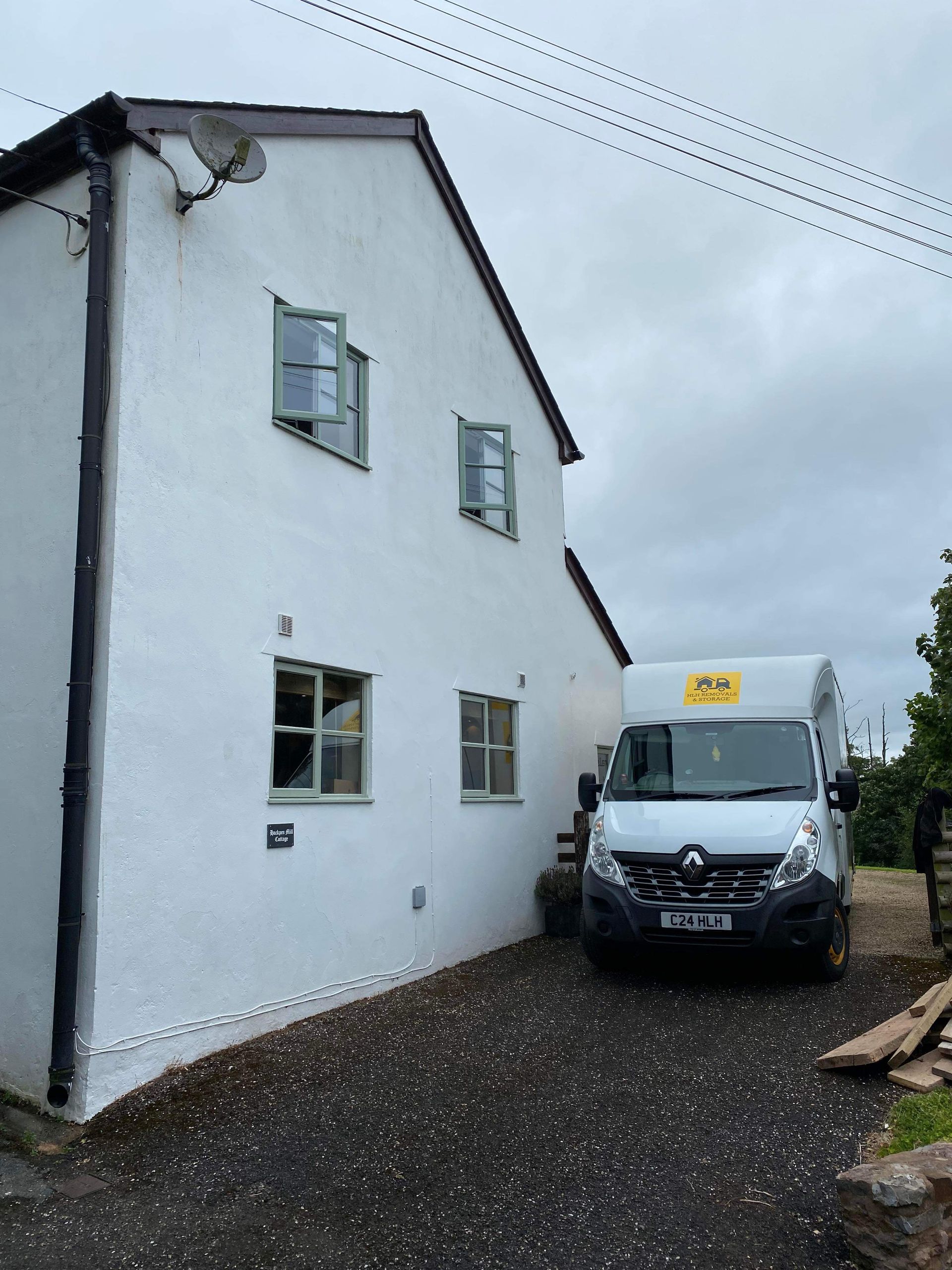 White two-story house beside a parked delivery van on a gravel driveway under a cloudy sky