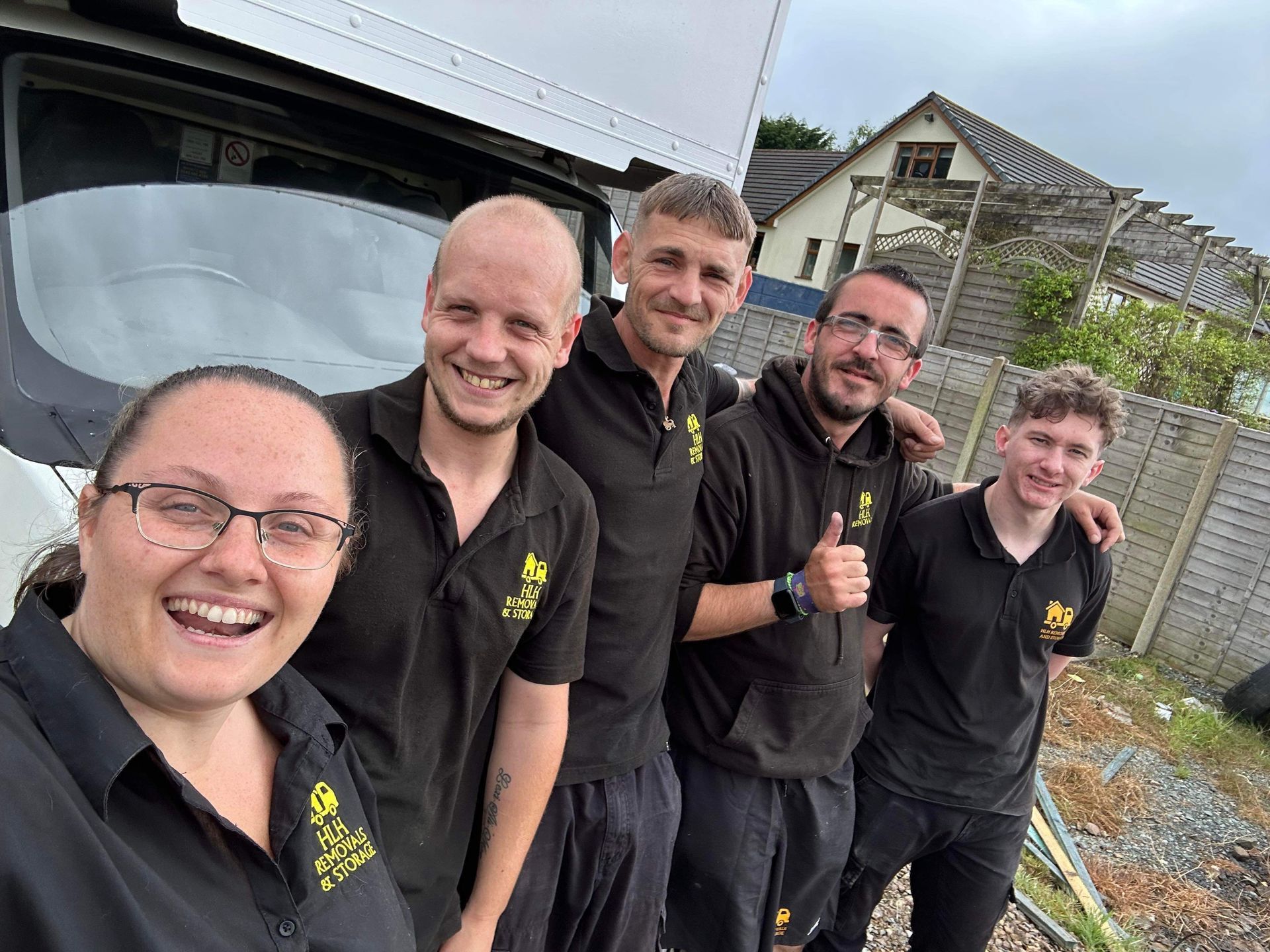 Five people in black polo shirts smiling outdoors beside a vehicle and fence