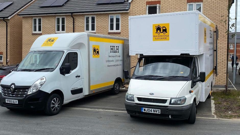 Two white delivery vans parked outside suburban houses on a wet residential street.
