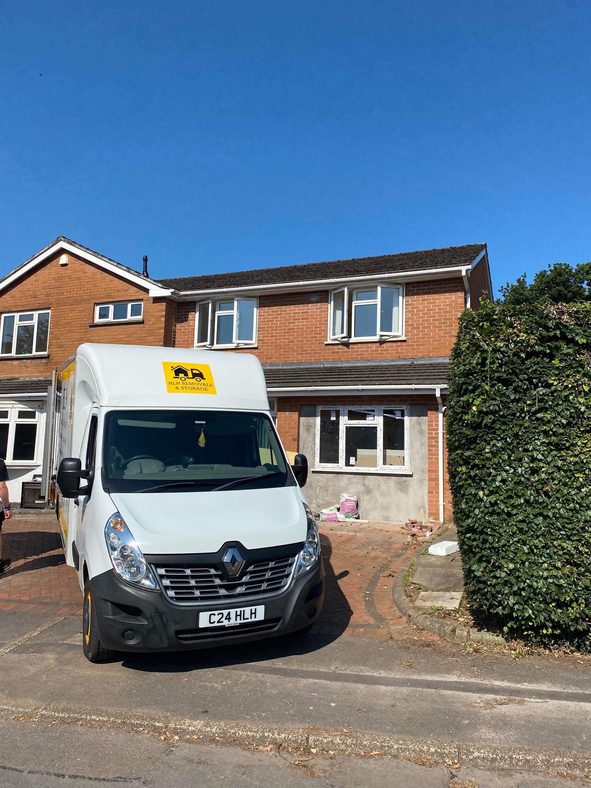 White delivery van parked outside a brick house on a sunny residential street.