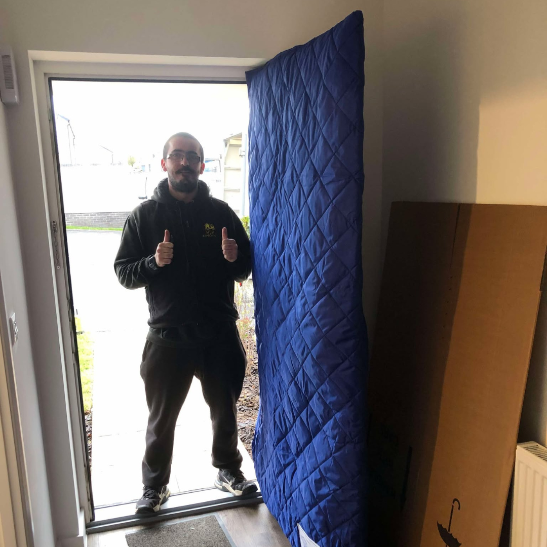 Person standing in a doorway giving two thumbs up, with a blue padded door panel beside them.