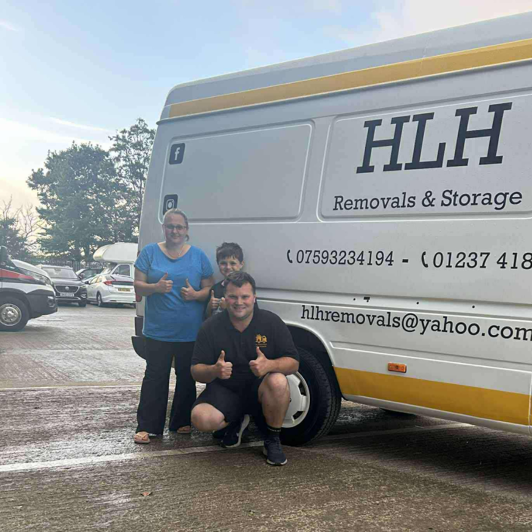 Two people posing beside an HLH Removals & Storage van in a parking lot