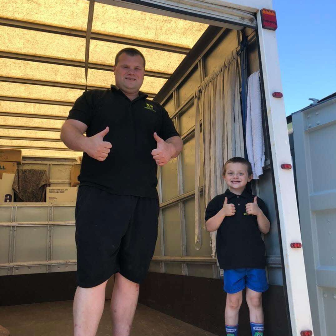 Two people smiling and giving thumbs up in the back of a truck or trailer.
