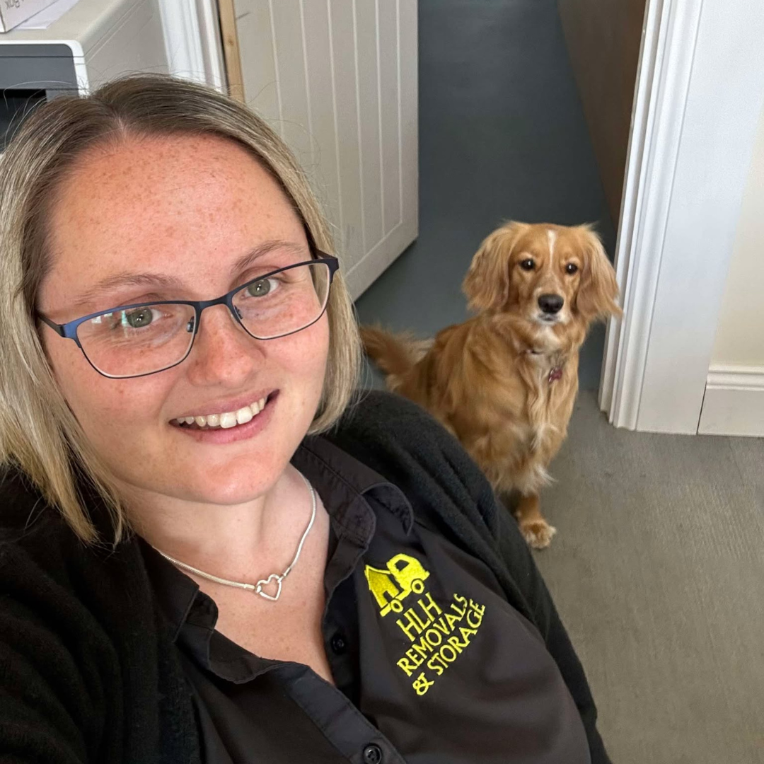 Smiling person wearing glasses with a golden dog sitting in a hallway