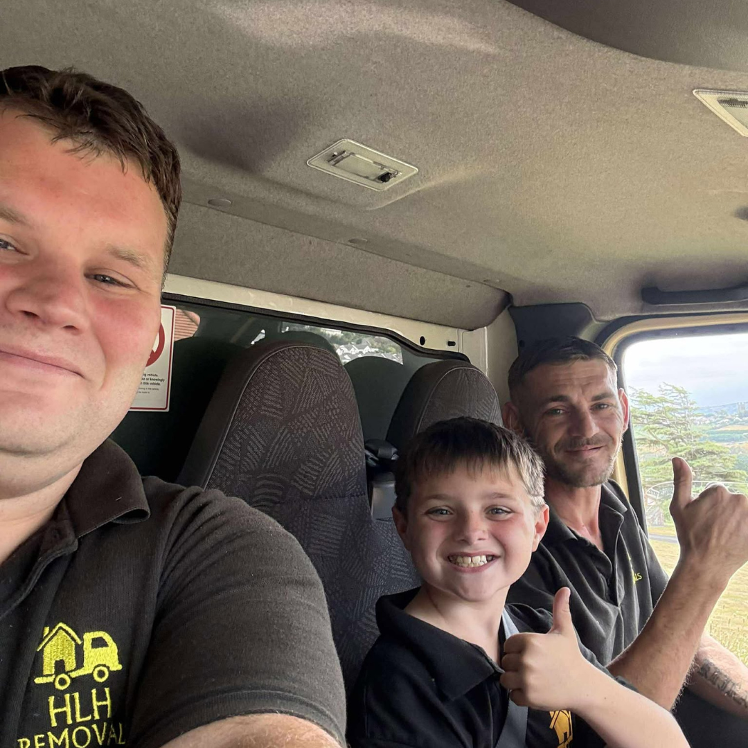 Three smiling people inside a vehicle, posing with thumbs up on a sunny drive