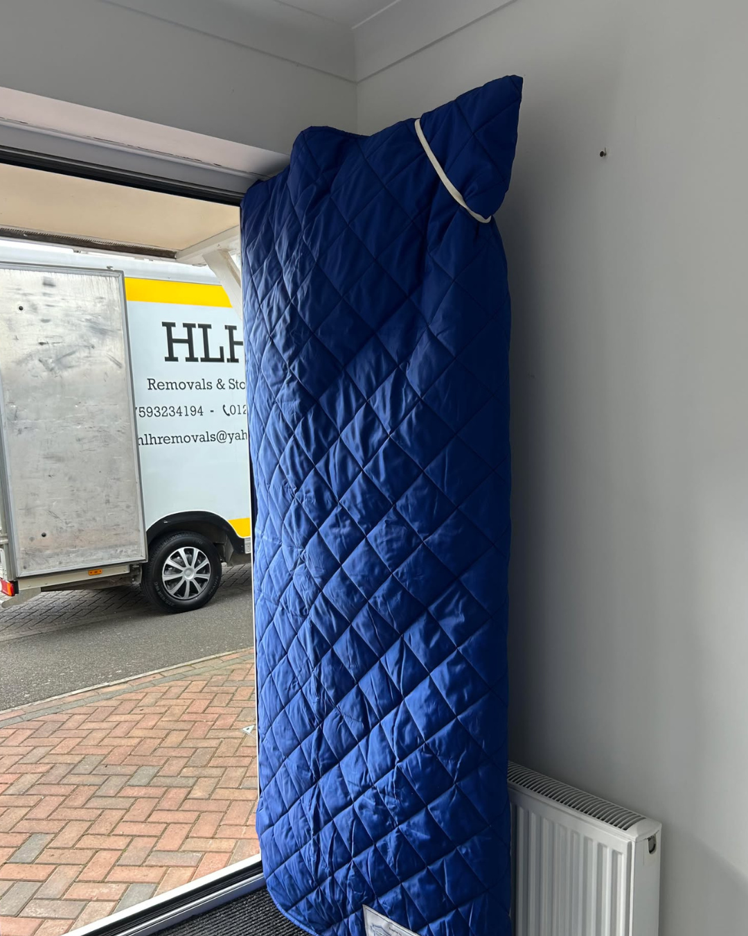 Blue quilted mattress or padded cover hanging in a doorway beside a radiator.