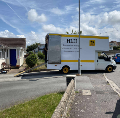 White HLH moving truck parked on a quiet residential street beside houses under a cloudy sky
