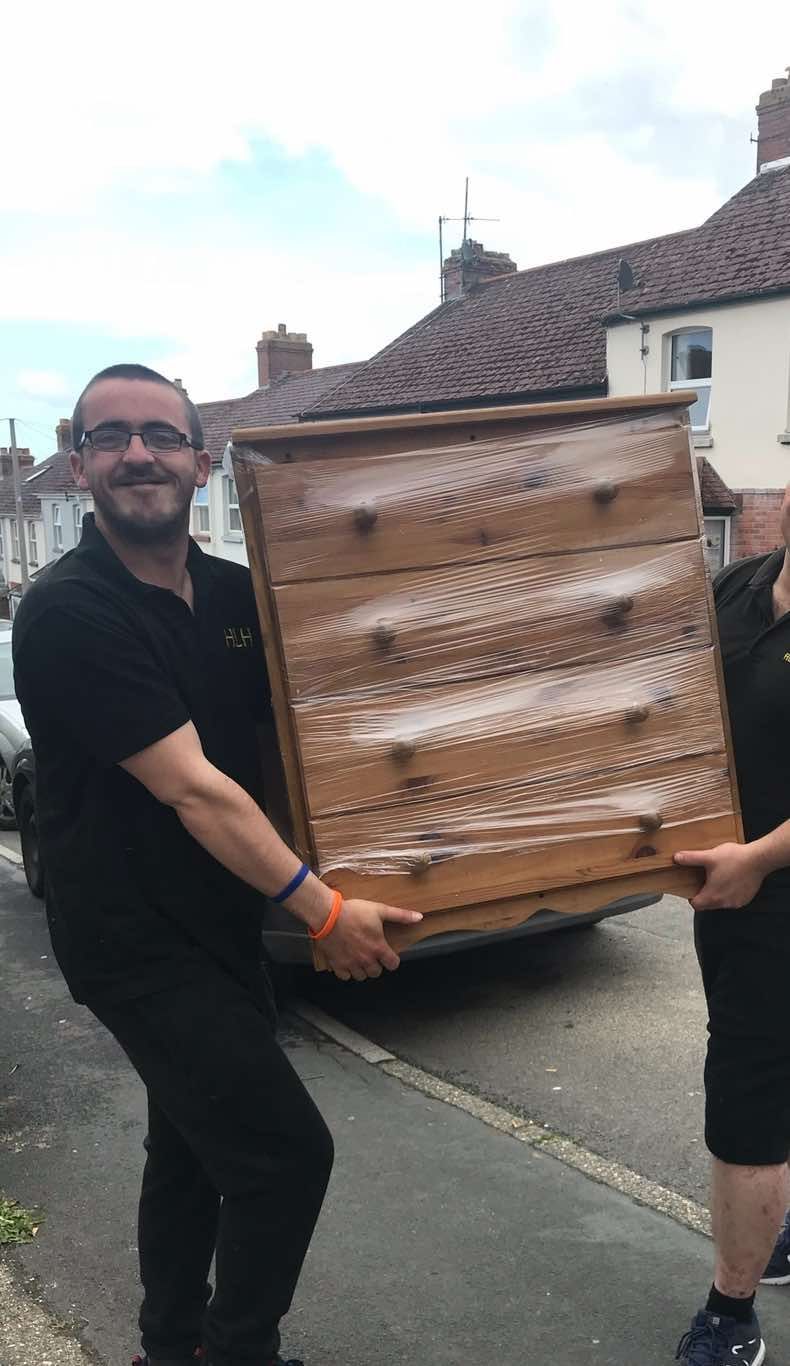 Two people carrying a large wooden beehive box on a residential street.