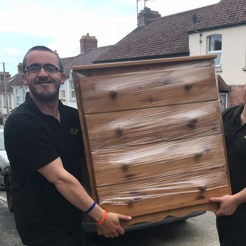 Two men carrying a wrapped wooden dresser outside a house on a street