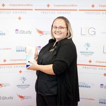 Woman smiling at a corporate awards backdrop, holding a trophy.