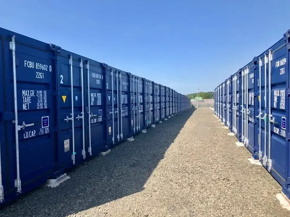 Rows of blue shipping containers lining a gravel path under a clear sky