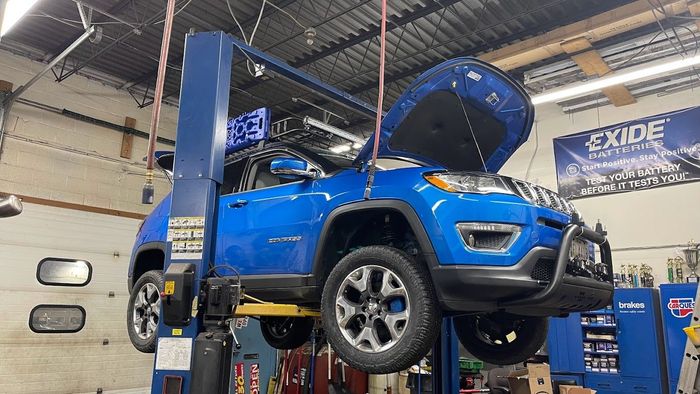 A blue jeep compass is sitting on a lift in a garage.