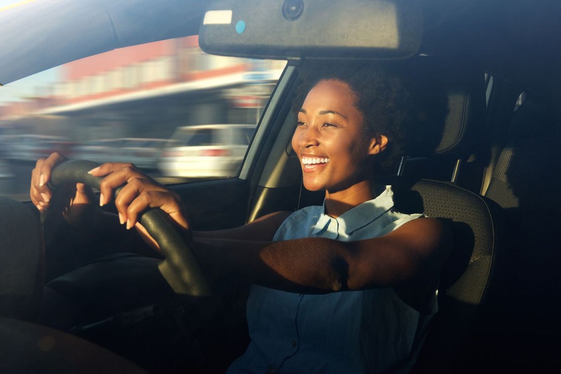 A woman is smiling while driving a car on a highway.