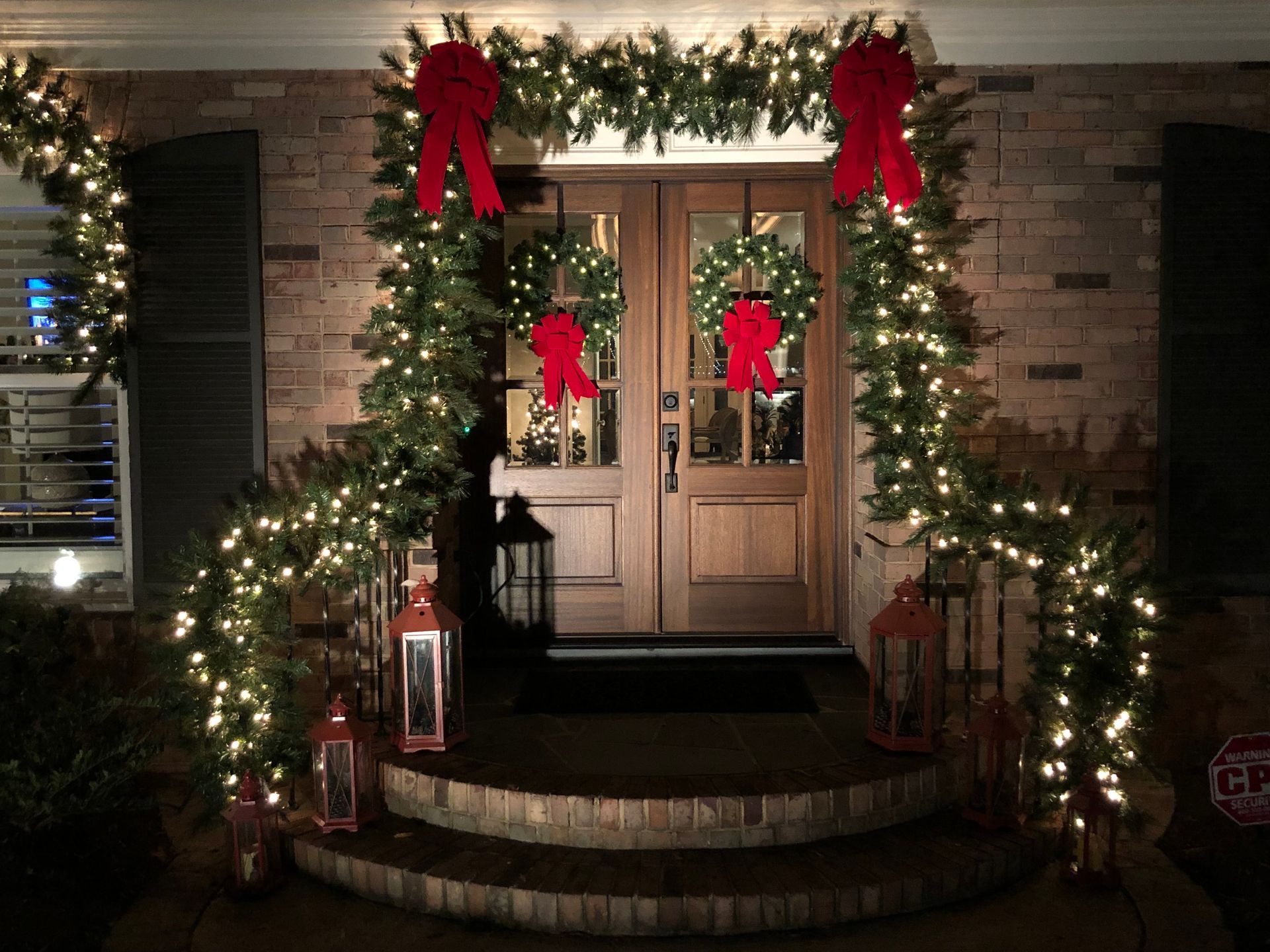 Festive Christmas decorations on a front porch. Green garland with lights and red bows around the door and steps.