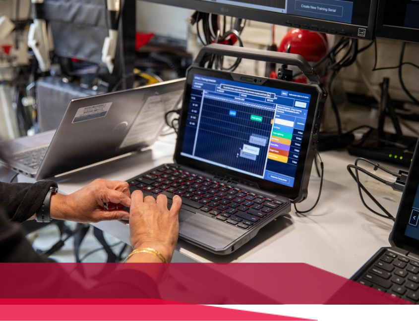 Hands typing on a laptop with a screen displaying data, other electronics in the background.