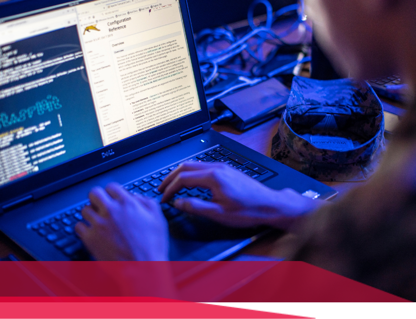 Person typing on a laptop with code displayed, lit by blue light.