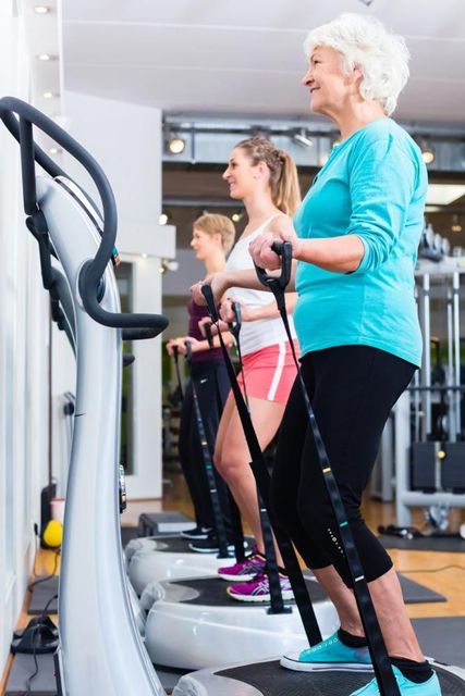 Three women exercising on vibration platforms in a gym, smiling.