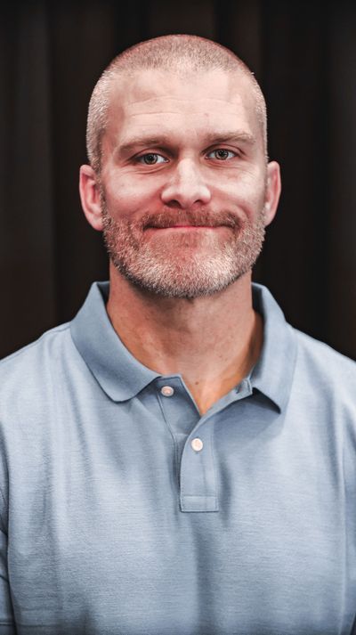 A man with a beard is wearing a blue polo shirt and smiling.