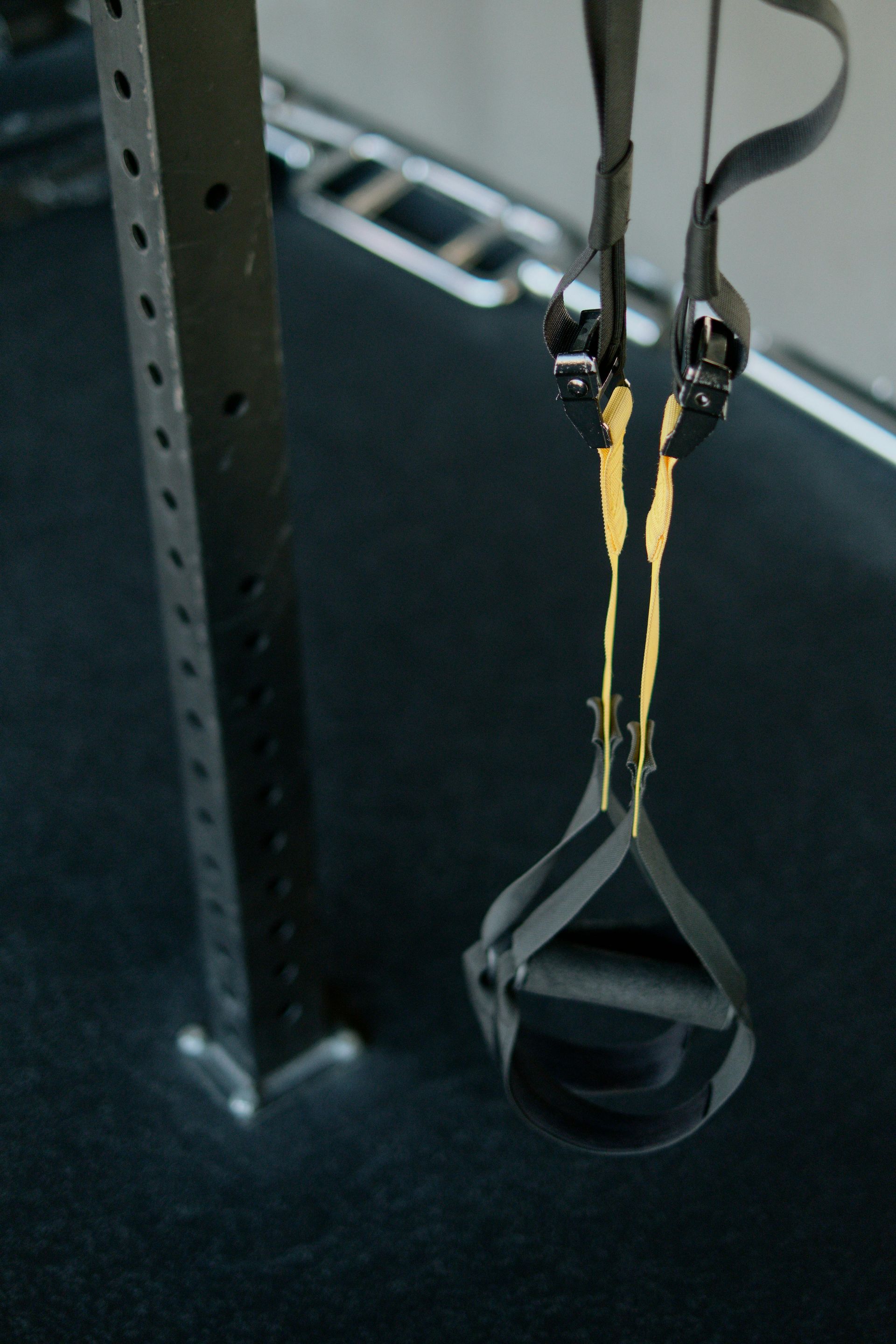 Black exercise straps hanging from a metal beam, set on a dark surface.