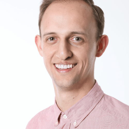 Portrait of a smiling person in a light pink button-up shirt against a white background