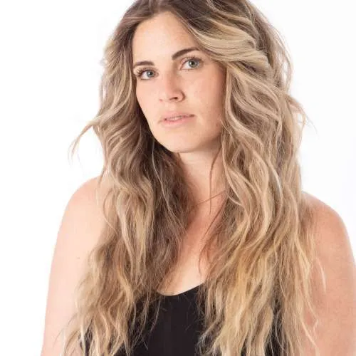 Portrait of a blonde woman with wavy hair wearing a black top against a white background